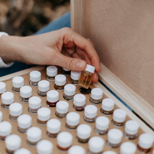 Coffret en bois ouvert contenant plusieurs échantillons d'huiles essentielles. Avec la main de Julie en sélectionnant une.